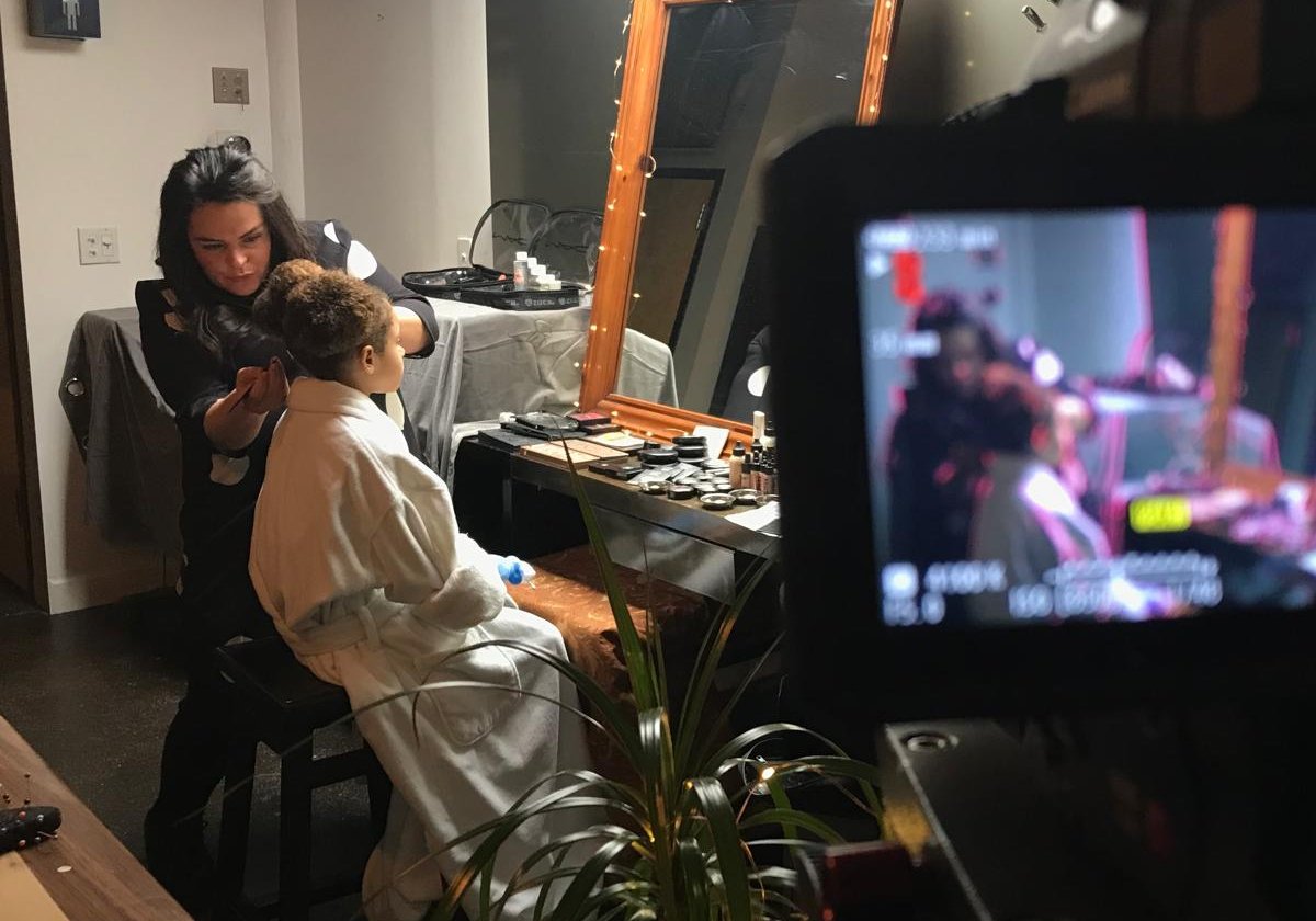 Nadia Veenhof doet het haar van een model op de set, met de camera in beeld